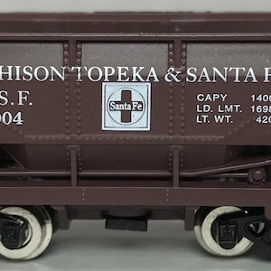 May include: A brown model train car with the text "ATCHISON TOPEKA & SANTA FE" and "A.T.S.F. 782004". The car has a Santa Fe logo and the text "CAPY 140000, LD. LMT. 169800, LT. WT. 42000". The train car has four wheels and is a miniature replica.