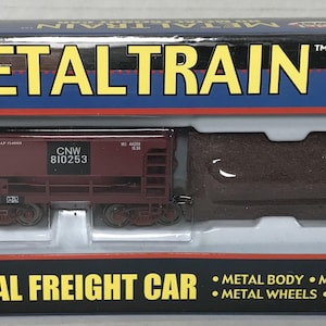 May include: A red and black HO scale model train freight car with the letters CNW and the number 810253 printed on the side. The car is made of metal and has metal wheels and axles. The packaging says "Metal Train" and "Model Power".
