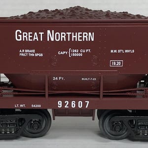 May include: A maroon Great Northern model train car filled with a dark brown substance. The car has black wheels and the text "Great Northern" in white. It also has the number 92607 and the text "Be Careful".