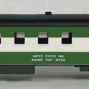 May include: Green and white model train car with black roof and "UNITED STATES MAIL RAILWAY POST OFFICE" printed on the side. The car is numbered 403.