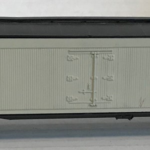 May include: A white boxcar with black trim and a red CN logo. The boxcar has a black roof and a single door on the side. The boxcar is on a model train track.