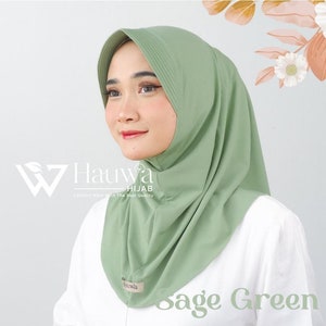 May include: Sage green hijab with a pleated design. The hijab is made of a soft, comfortable fabric and has a simple, elegant style. The text "Hauwa HIJAB" is visible on the left side of the image.