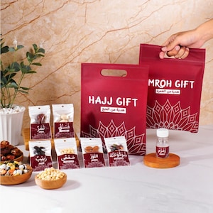 Puede incluir: Una colección de regalos de Hajj, que incluye pequeñas bolsas de dátiles, nueces y chocolates, junto con una botella de agua de Zamzam. Los regalos se presentan en bolsas rojas con texto y diseños blancos.