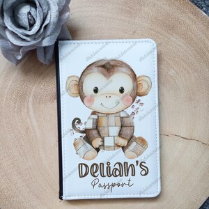 May include: White passport holder featuring a brown monkey wearing a plaid shirt. The text "Delian's Passport" is printed on the front.
