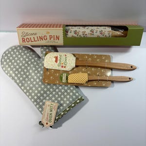 May include: A kitchen set including a silicone rolling pin in a box, a gray and white checkered oven mitt with a tag, and two wooden-handled silicone spatulas on a floral backing card. The spatulas feature the text Baked with Love.