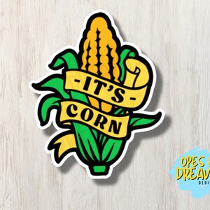 Può includere: Una pannocchia di mais gialla con foglie verdi e uno striscione che dice "It's Corn" in lettere nere. Lo striscione è giallo con un contorno bianco.