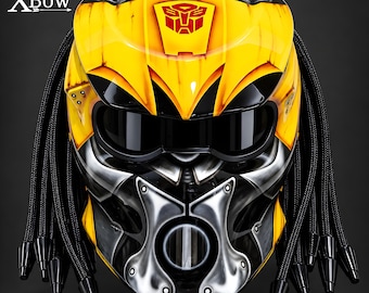 May include: A yellow and black motorcycle helmet featuring a red Autobot logo on the forehead, a dark visor, and black braided dreadlocks on the sides. The helmet has a metallic silver faceplate design and the text XBow printed in the top left corner.
