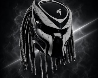 May include: A black and white motorcycle helmet featuring a stylized, aggressive design with a smooth, glossy finish. The helmet includes long, braided, cord-like attachments hanging from the sides and back, resembling dreadlocks, with a sleek visor.