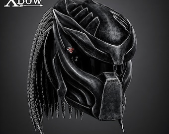 May include: A black motorcycle helmet with a textured, weathered finish and a sculpted, angular design. It features a dark visor, small red accents on the side, and long, braided black cords extending from the back. The text XBow is visible.