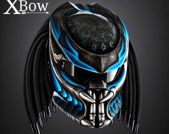 May include: A motorcycle helmet featuring a dark metallic finish with bright blue accents and a Predator-inspired design. The helmet includes black braided dreadlocks on the sides, a dark visor, and the text XBow printed in the upper left corner.