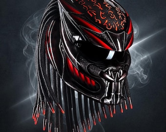 May include: A black motorcycle helmet featuring a red and black patterned design with a dark visor. The helmet includes long black braided cords hanging from the back, each tipped with a pointed red accent, and intricate red markings on the top.