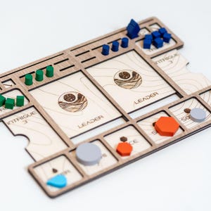 May include: Wooden board game with various coloured game pieces. The board has spaces for cards labelled "Leader" and "Intrigue". There are blue, green, orange, and grey game pieces. The game board has a light wood finish.