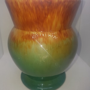 May include: A green and brown ceramic vase with a flared top and a round base. The vase has a gradient glaze, transitioning from a rich brown at the top to a vibrant green at the bottom.