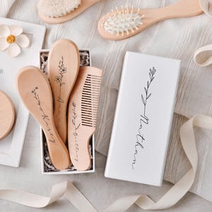 May include: A white box with a floral design and the name "Northam" printed on it. The box contains four wooden hair brushes with floral designs and names "Avery", "Kinsey", "Brittany" and "Northam" engraved on them.