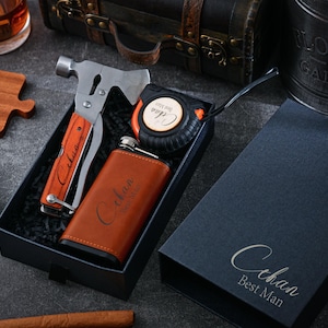 Könnte beinhalten: Ein Geschenkset in einer schwarzen Box mit einer braunen, lederbezogenen Flasche, einem Multitool mit Hammer und Messer sowie einem Maßband. Die Flasche und das Maßband tragen den Namen "Cihan". Eine separate schwarze Box ist ebenfalls vorhanden, mit der Aufschrift "Cihan Best Man".