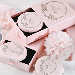 以下が含まれることがあります： ピンクの箱に花柄のデザインと「bridesmaid」の文字が書かれたコンパクトミラーが入っています。ミラーは花柄のピンクの箱に入っています。