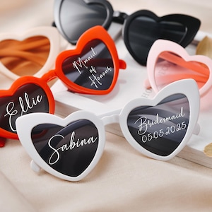 Puede incluir: Gafas de sol con forma de corazón en varios colores: rojo, blanco, negro y rosa. Algunas gafas tienen texto personalizado, como nombres y fechas. Un accesorio divertido.