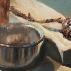 May include: A close-up of a silver metal pot with a brown wooden board and a brown pine cone in the background.