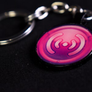 May include: A pink and purple keychain with a stylised Wi-Fi symbol. The keychain is attached to a silver key ring.