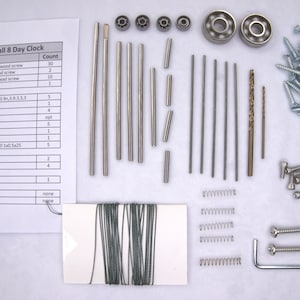 May include: A kit for building a small 8-day clock. The kit includes various metal parts, screws, springs, and a small spool of string. The parts are laid out on a white surface. The kit also includes a list of parts and their quantities.