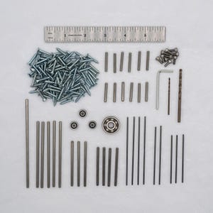 Puede incluir: Un kit de ferretería que contiene un montón de tornillos plateados, varias varillas metálicas de distintas longitudes, tres rodamientos pequeños, un rodamiento grande, pernos pequeños, una llave hexagonal y dos brocas, con una regla de 15 cm.