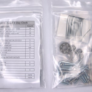 K&ouml;nnte beinhalten: Eine transparente Plastikt&uuml;te mit den Teilen f&uuml;r ein kleines 8-Tage-Uhr-Set. Die Teile umfassen Schrauben, D&uuml;bel, eine Edelstahlstange, einen Inbusschl&uuml;ssel, einen Bohrer, Federn, Kugellager und Angelschnur. Die T&uuml;te enth&auml;lt auch eine Liste der Teile und ihrer Mengen.