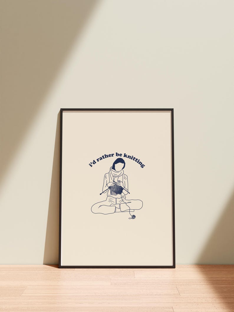 Pu&ograve; includere: Una stampa incorniciata nera con sfondo bianco e un'illustrazione blu di una persona che fa la maglia. Il testo "I'd rather be knitting" &egrave; scritto in blu in corsivo.