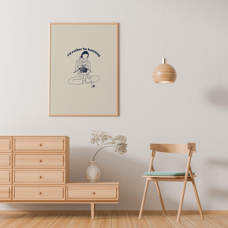 Pu&ograve; includere: Una stampa incorniciata con uno sfondo beige e un'illustrazione blu di una persona che fa la maglia. Il testo "I'd rather be knitting" &egrave; scritto in blu sopra l'illustrazione.