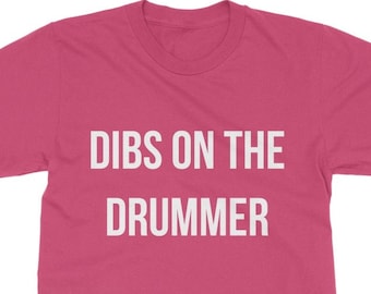 Puede incluir: Camiseta rosa con texto blanco que dice "DIBS ON THE DRUMMER".
