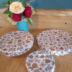Puede incluir: Tres cubiertas reutilizables para alimentos con un estampado floral en tonos rosa, naranja y azul sobre un fondo blanco. Un peque&ntilde;o jarr&oacute;n turquesa contiene un ramo de flores con rosas blancas y rojas. Las cubiertas son de diferentes tama&ntilde;os.
