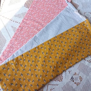 Puede incluir: Tres piezas de tela rectangulares con diferentes estampados. Una es rosa con pequeñas flores blancas, otra es azul claro con hojas blancas y la última es amarillo mostaza con siluetas de pájaros.
