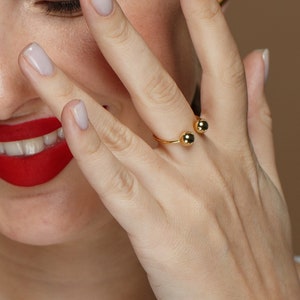 May include: A gold ring with two round balls on the ends. The ring is worn on a person's finger.