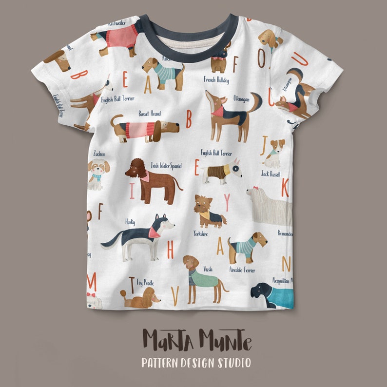 May include: White short-sleeved t-shirt with an illustrated alphabet featuring different dog breeds, each with a letter. The shirt has a dark grey neckline and the words "MARTA MUNTE" and "PATTERN DESIGN STUDIO" at the bottom.