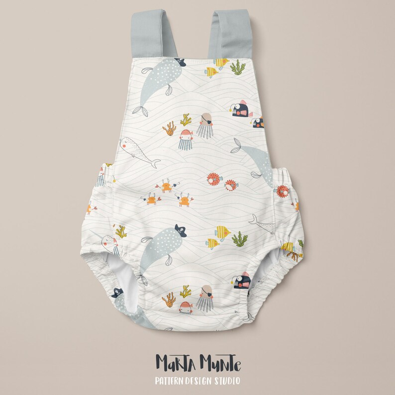 May include: White baby romper with a whimsical ocean-themed pattern featuring whales, fish, crabs, and jellyfish. The romper has light blue straps and is decorated with the text "Marta Munte Pattern Design Studio".