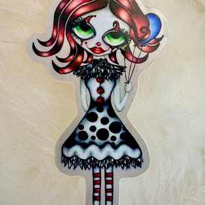 May include: A sticker featuring a stylized illustration of a clown girl with red hair, green eyes, and a polka-dot dress. She holds blue balloons and has red and white striped stockings.