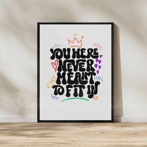 May include: A black and white printable wall art print with the text "You were never meant to fit in" in a colorful, retro font. The text is surrounded by stars, hearts, and a crown.