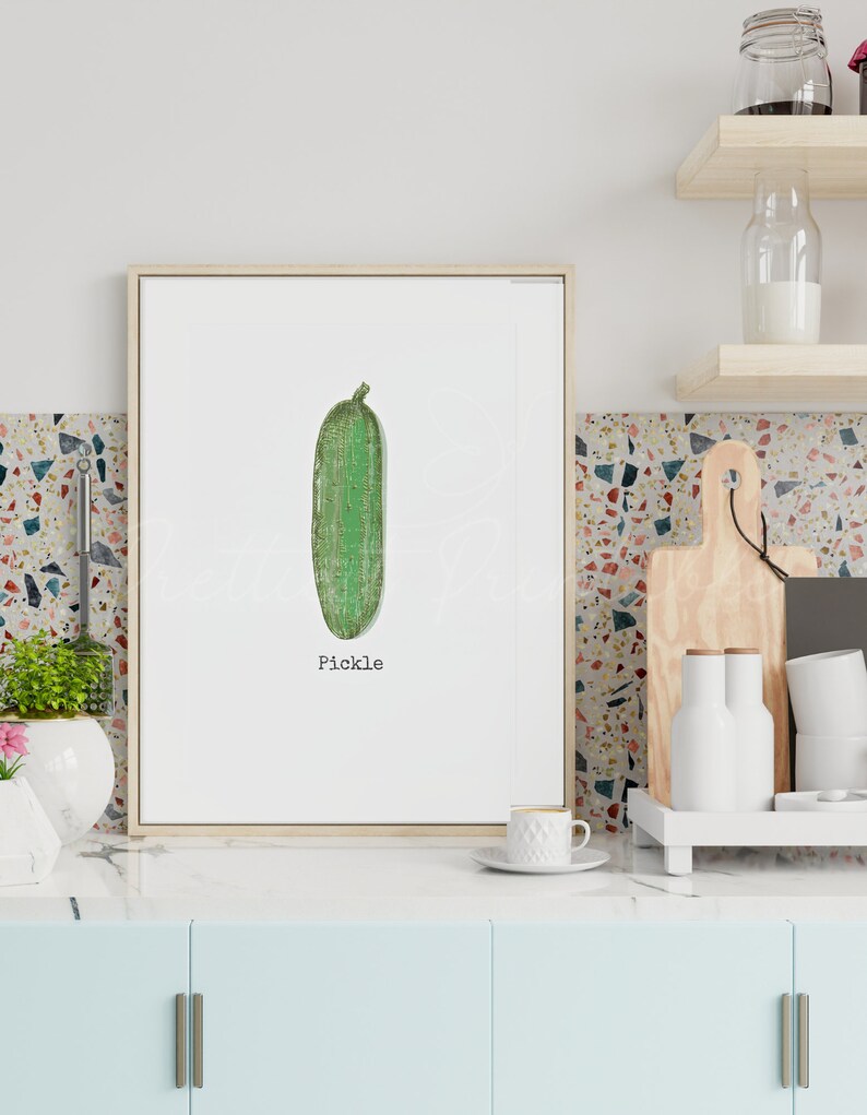 May include: A framed print of a green pickle with the word "Pickle" printed below it. The print is hanging on a wall in a kitchen.