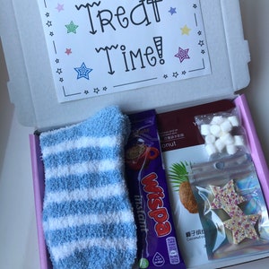 May include: A gift box containing a blue and white striped fluffy sock, a Cadbury Wispa instant hot chocolate sachet, marshmallows, star-shaped biscuits, and a card that reads "Treat Time!" with star accents.