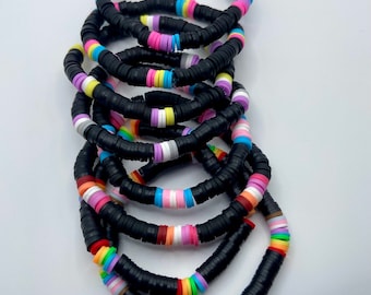 May include: A stack of colorful bracelets made with black and multi-colored beads. The bracelets feature a variety of colors, including pink, blue, yellow, green, and white.