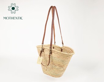 May include: A natural straw tote bag with brown leather straps and a brass buckle. The bag is large and has a wide opening.