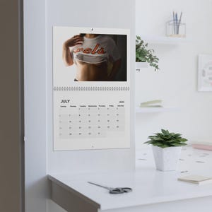 May include: A white calendar with a July 2025 calendar on the bottom half and a photo of a person wearing a white shirt with the word "cool" printed on it in orange letters on the top half.