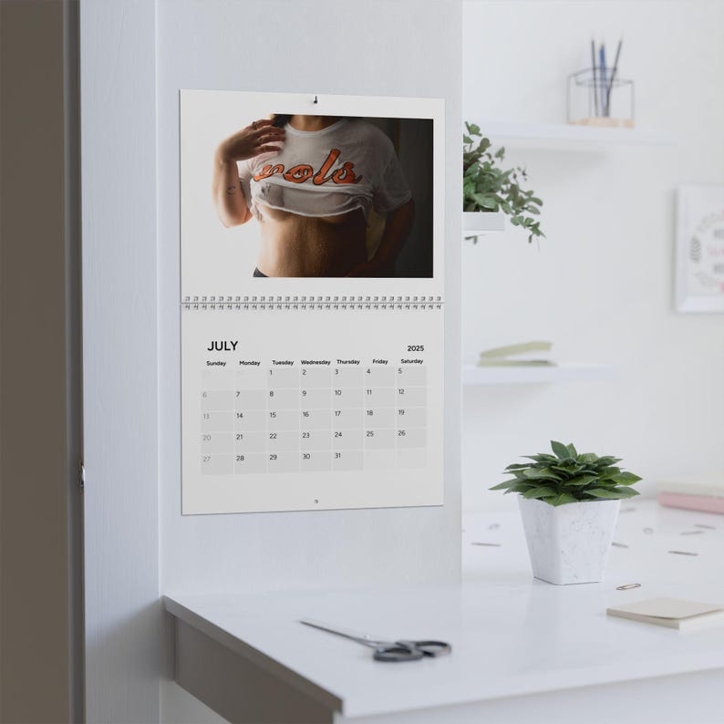 May include: A white calendar with a July 2025 calendar on the bottom half and a photo of a person wearing a white shirt with the word "cool" printed on it in orange letters on the top half.