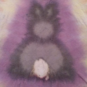 Puede incluir: Una tela de teñido anudado con una imagen descolorida de un conejo en tonos de morado, gris y blanco.