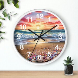 May include: White round clock with a beach scene and seashells. The clock face has black hands and white numbers. The background shows a sunset over the ocean with waves crashing on the shore.