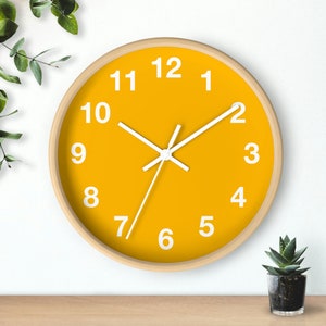 Può includere: Un orologio rotondo giallo con numeri e lancette bianchi. Il quadrante dell'orologio ha una cornice in legno.
