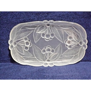 May include: An oval-shaped clear glass tray featuring a frosted relief pattern of clusters of cherries and detailed leaves. The decorative dish has a scalloped edge and a smooth, translucent surface with raised textures depicting fruit motifs.