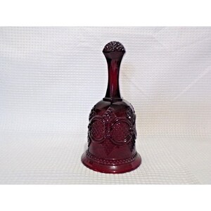 Peut inclure: Une cloche en verre rouge rubis avec une longue poignée fine et un dessus texturé. Le corps de la cloche présente un motif orné de cercles et de motifs floraux, pour un look vintage.
