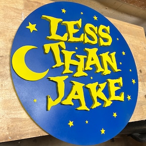 May include: A blue circular sign with a yellow crescent moon and stars. The sign says "Less Than Jake" in yellow 3D letters.