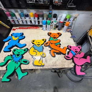 May include: Four dancing bear cutouts in bright colors. One is blue with a yellow chest, one is green with a blue chest, one is yellow with a blue chest, one is orange with a green chest, and one is pink with a blue chest, all with black outlines.