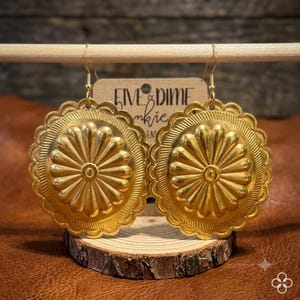 May include: A pair of gold-toned circular earrings featuring a scalloped edge and a central sunburst or floral embossed pattern. The earrings hang from gold-toned hooks and are displayed in front of a tan card with the text Five & Dime Junkie.